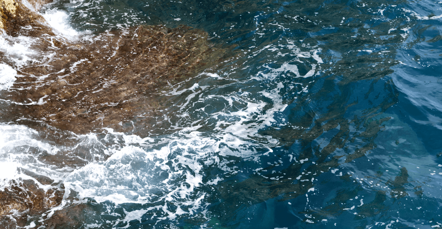 Vue en plongée de vagues avec écume blanche se brisant contre des rochers escarpés par beau temps.